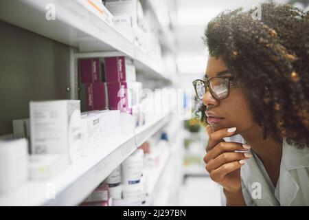 This little guy seems to be lost. Shot of a focused young female pharmacist looking closely at medication on a shelf inside a pharmacy. Stock Photo