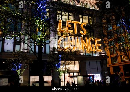 London, UK. 30th Mar, 2022. A view of a lit sign 'Let's change' on the wall of Selfridges on Bond street. Trees on the side of Bond street are lit with blue and yellow lights to show solidarity with Ukraine. Credit: SOPA Images Limited/Alamy Live News Stock Photo