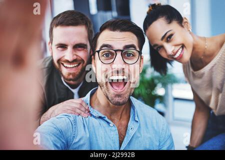 Theyre one cheerful and optimistic team. Shot of a group of designers taking selfies together in an office. Stock Photo