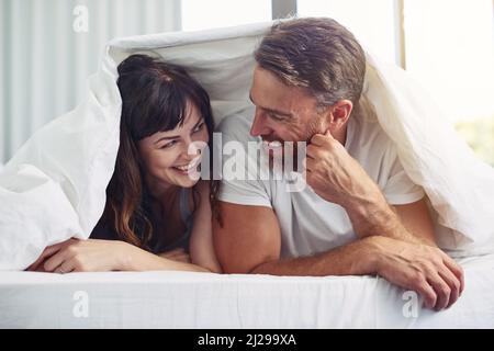 So nice of you to join me. Shot of a cheerful young couple crawling out of bed while having a laugh together during morning hours. Stock Photo