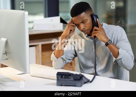 Delivering bad news is a tough call to make. Shot of a young man using a phone and looking stressed in a modern office. Stock Photo