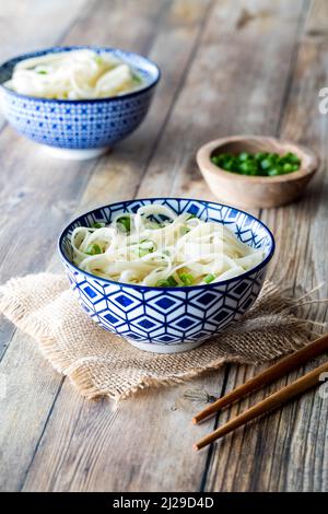 Bowls of noodles on a wooden table, garnished with green onion. Stock Photo