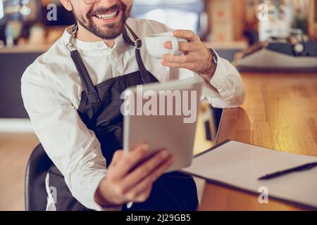 Cheerful man drinking coffee and using tablet computer in cafe Stock Photo