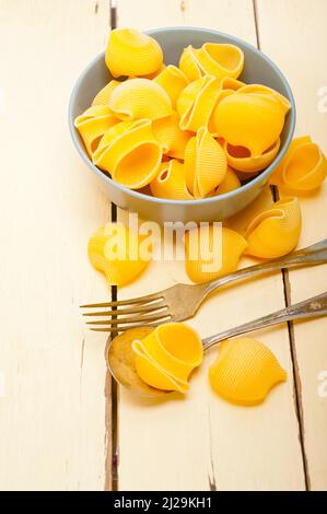 Raw Italian snail lumaconi pasta on a blue bowl over rustic table macro Stock Photo