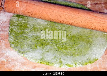 Pasta dough with spinach, is rolled out with a rolling pin Stock Photo