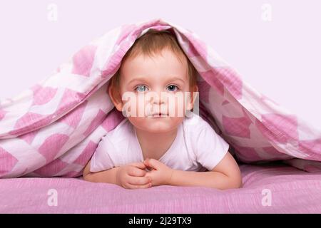 Little caucasian boy hiding under pink blanket. Stock Photo