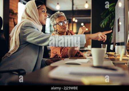 Two diverse businesswomen having a discussion while looking at a computer screen in an office. Creative businesswomen working as a team in a modern co Stock Photo