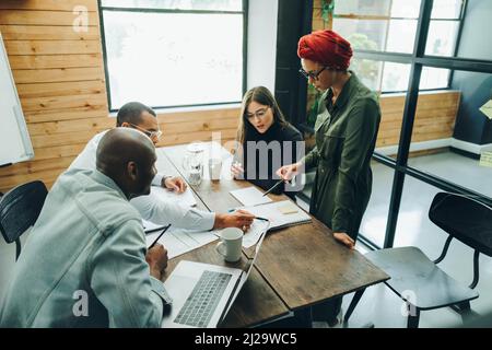 Multicultural business team discussing a report document during a boardroom meeting. Group of creative businesspeople sharing strategic ideas in an in Stock Photo