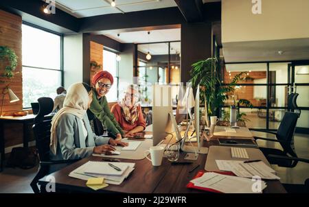 Happy businesswomen working together in a modern co-working office. Group of multicultural businesswomen smiling cheerfully while having a discussion Stock Photo