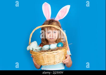 Bunny boy with easter basket isolated on blue background. Kids boy in bunny ears hunting easter eggs. Easter egg hunt. Funny kids face. Stock Photo