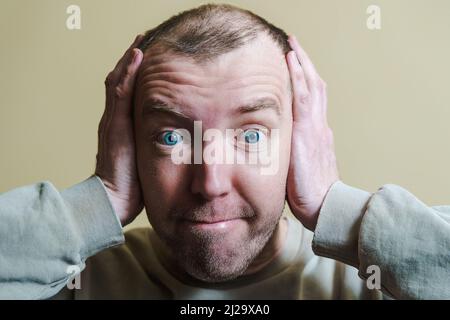 The man covers his ears with his hands. Portrait of a young man making faces. Stock Photo
