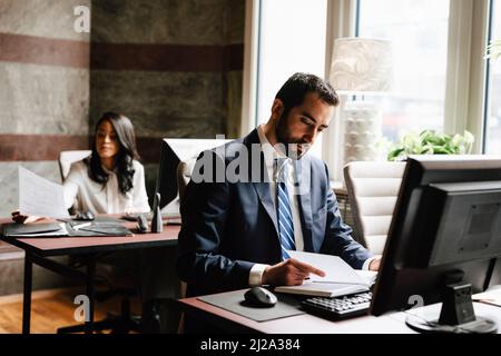 Confident male lawyer reading diary with female colleague working in background at office Stock Photo