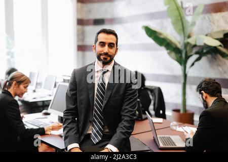 Portrait of bearded businessman sitting on desk in office Stock Photo