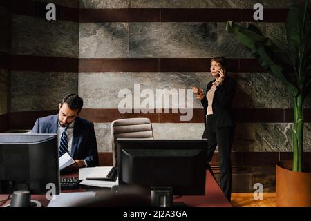 Businesswoman talking on smart phone while male colleague working at law office Stock Photo