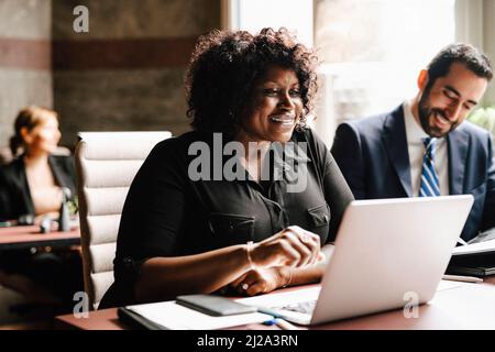 Smiling businesswoman using laptop by businessman sitting at desk working in law office Stock Photo