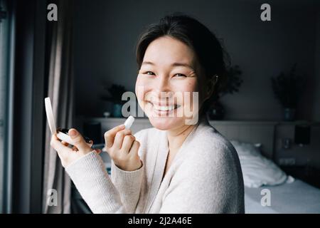 Portrait of happy woman applying make-up in bedroom at home Stock Photo