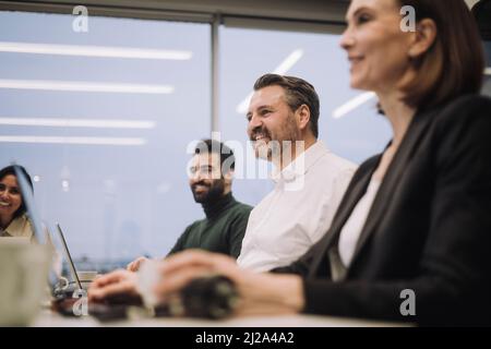 Smiling businesswoman with male and female colleagues discussing while working at office Stock Photo