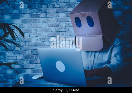 Anonymous hacker use laptop computer and connection at home wearing a box on his head to be not recognize. Concept of cyber crime and privacy protecti Stock Photo