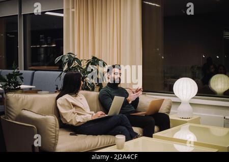 Businessman explaining strategy to female colleague while working late in office at night Stock Photo