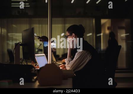 Ambitious businesswoman using laptop while working late in office at night Stock Photo