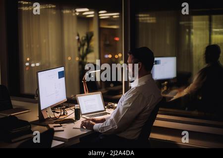 Businessman typing on computer keyboard while working in office at night Stock Photo