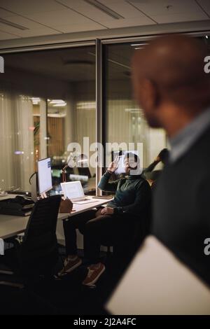 Businessman talking with male colleague while working overtime in office at night Stock Photo