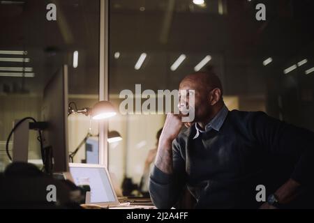 Ambitious working man using computer while working overtime at work place Stock Photo