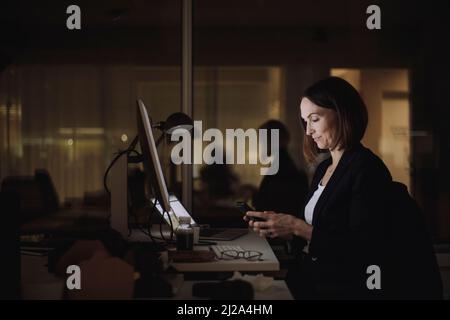 Businesswoman using smart phone while working overtime at work place Stock Photo