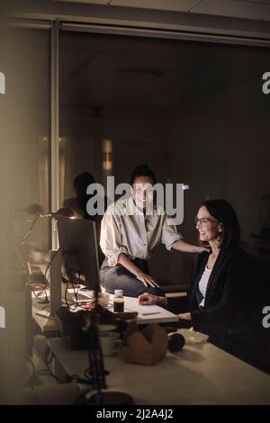 Smiling female colleagues discussing on computer while working last minute at work place Stock Photo