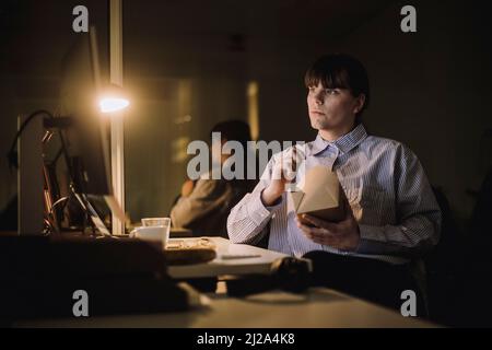 Businesswoman with food box working late in office at night Stock Photo