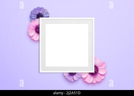Blank picture frame surrounded with flowers on purple surface. Top view, flat lay composition Stock Photo