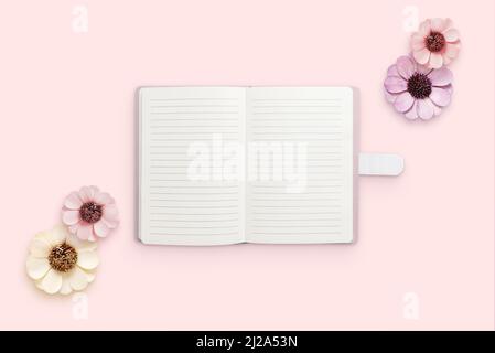 Notepad surrounded by flowers on pink surface. Blank papers for text. Flat lay, top view composition Stock Photo