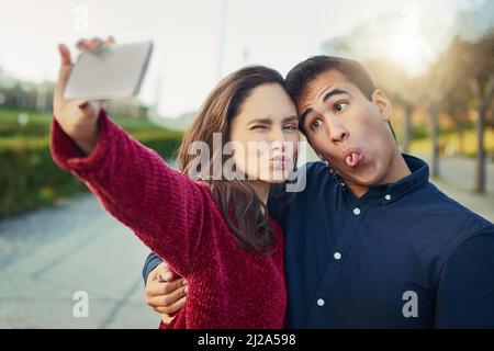 I found my soulmate in silliness. Shot of a young couple making funny faces while taking a selfie outdoors. Stock Photo