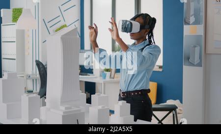 Woman architect wearing vr glasses to design construction layout and building model. Builder planning real estate project with virtual reality headset and maquette. Architecture plan Stock Photo