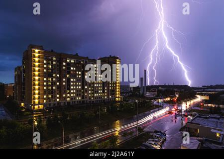 A lightning strike during a thunderstorm against the background of a city building. Night city traffic. Stock Photo