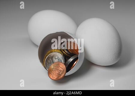 Two whole and one broken white chicken eggs and American cents that fell out of them Stock Photo