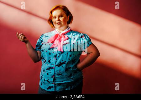 smiling young woman portrait in studio over pink background redhead ginger Stock Photo