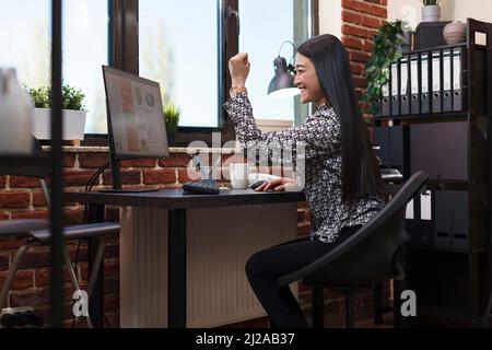 Overjoyed project manager celebrating job promotion and successful deal by vigorously raising hand. Happy motivated office worker satisfied by good results of promoting campaign. Stock Photo