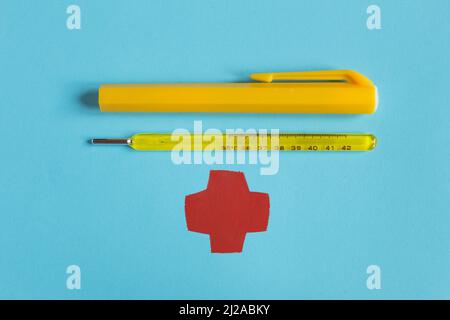 Vintage yellow mercury thermometer with its case next to it on the textured blue paper background and a drawing of a medical emblem in the shape of a Stock Photo
