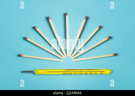 A group of matches ready to light forming a sun on top of a hot mercury thermometer on a colorful blue background. Conceptual photography, environment Stock Photo