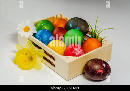 Easter composition, colorful, hand-painted eggs arranged in a small wooden box, still life on a light background, flowers Stock Photo