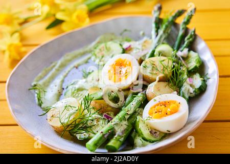 From above of yummy spring salad with ripe asparagus and boiled eggs with potatoes placed on table with flowers for lunch Stock Photo