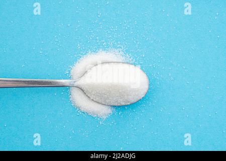 Close-up of a spoon with sugar heap, crystals of white sugar on blue background, top view Stock Photo