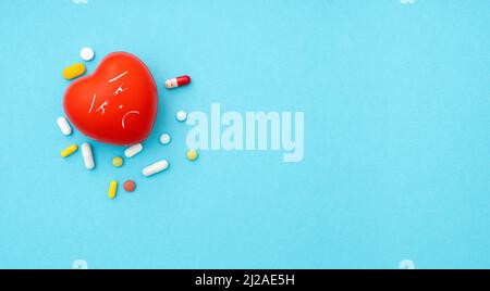 Shape of red heart with sad emotion and heap of pills on blue background, top view, space for text, concept picture about heart disease Stock Photo