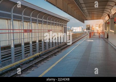 Surface metro station, stretching into distance, in rays of setting sun. Deserted platform, waiting for train. Vienna, Austria 03 2022 Stock Photo