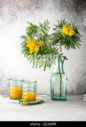 Beautiful bouquet of silver wattle or yellow mimosa flowers in turquoise glass vase on light rustic background. Still life. Stock Photo