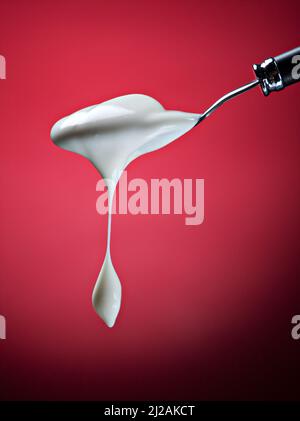 Spoon with natural yogurt over red background. Stock Photo