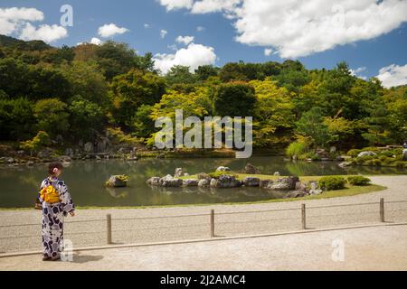Young woman, with her back facing, wearing a traditional yukata in the Japanese zen garden of the Tenryu-Ji Buddhist Temple, Arashiyama, Kyoto