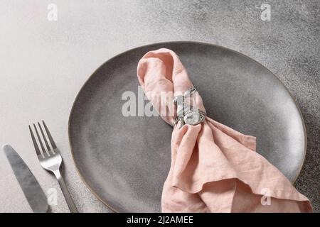 Easter dinner and table setting with pink decorations and rabbit as napkin ring on gray background. Close up. Copy space. Stock Photo