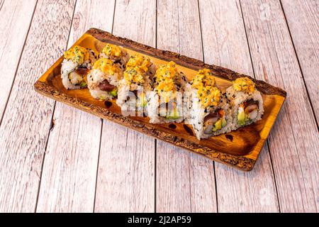 Sushi uramaki dragon roll with soy sauce, avocado, nori seaweed, red tuna, chives on a wooden plate Stock Photo